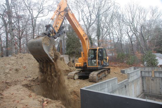 Using the excavator, George drops bucket loads of the material that he was able to save during exavation ...