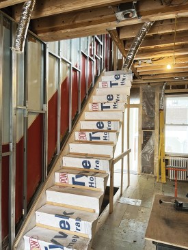 The staircase stringer was secured to the party wall with a double 2x6. The combined 4 1/8 inches leaves room for a 1-inch air space, steel studs, MLV, and 5/8-inch drywall.