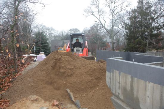 George pushes the first load of clean fill around the garage foundation using a skid steer machine.
