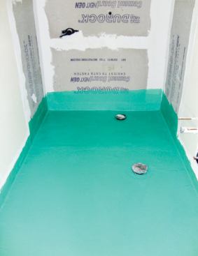 After removing it, the author lowered the concrete slab in the shower area by an inch, smoothed and sloped the surface toward the new drain, and waterproofed the entire bathroom floor with a liquid waterproofing membrane.
