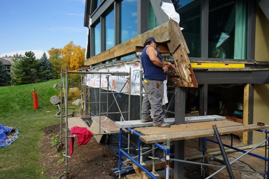 The crew has installed a temporary LVL beam installed across the face of the gable end to prevent the roof from spreading. Toby Bonilla of Great Lake Builders begins to strip the rotted end of the rafter  to expose a flitch beam that tied the A-frame-style gable together.  