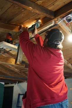 Next, they cut the roofing nails near the ridge board flush to the underside of the sheathing.  Note the laser installed just below the ridge; this will provide a reference line during the lifting. 
