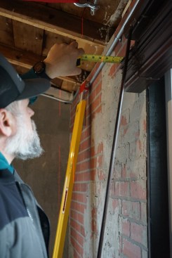 Measuring near the top and bottom of the outer wall to a laser that was set up to provide a reference plane, the author checks progress on the outer walls during the lift. (Note: The wood frames are covered with a faux-brick paneling.) 