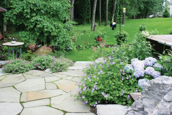 This patio is a continuation of the upper deck area, expanding the space for extra guests.The same stone was inlaid into the deck, creating uniformity between the upper and lower levels. Plantings are used to temper the hard surfaces.

