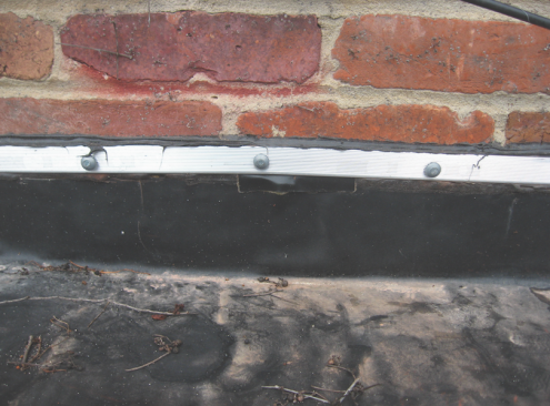 Critical-low slope details. At solid masonry walls, a termination bar (which will get lapped by a counterflashing let into the mortar joint) can work, but with brick veneer, only through-flashing will prevent leaks.