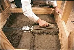 A bed of latex-modified mortar is troweled into the wire lath, using the float strips and the drain flange to gauge the slope.