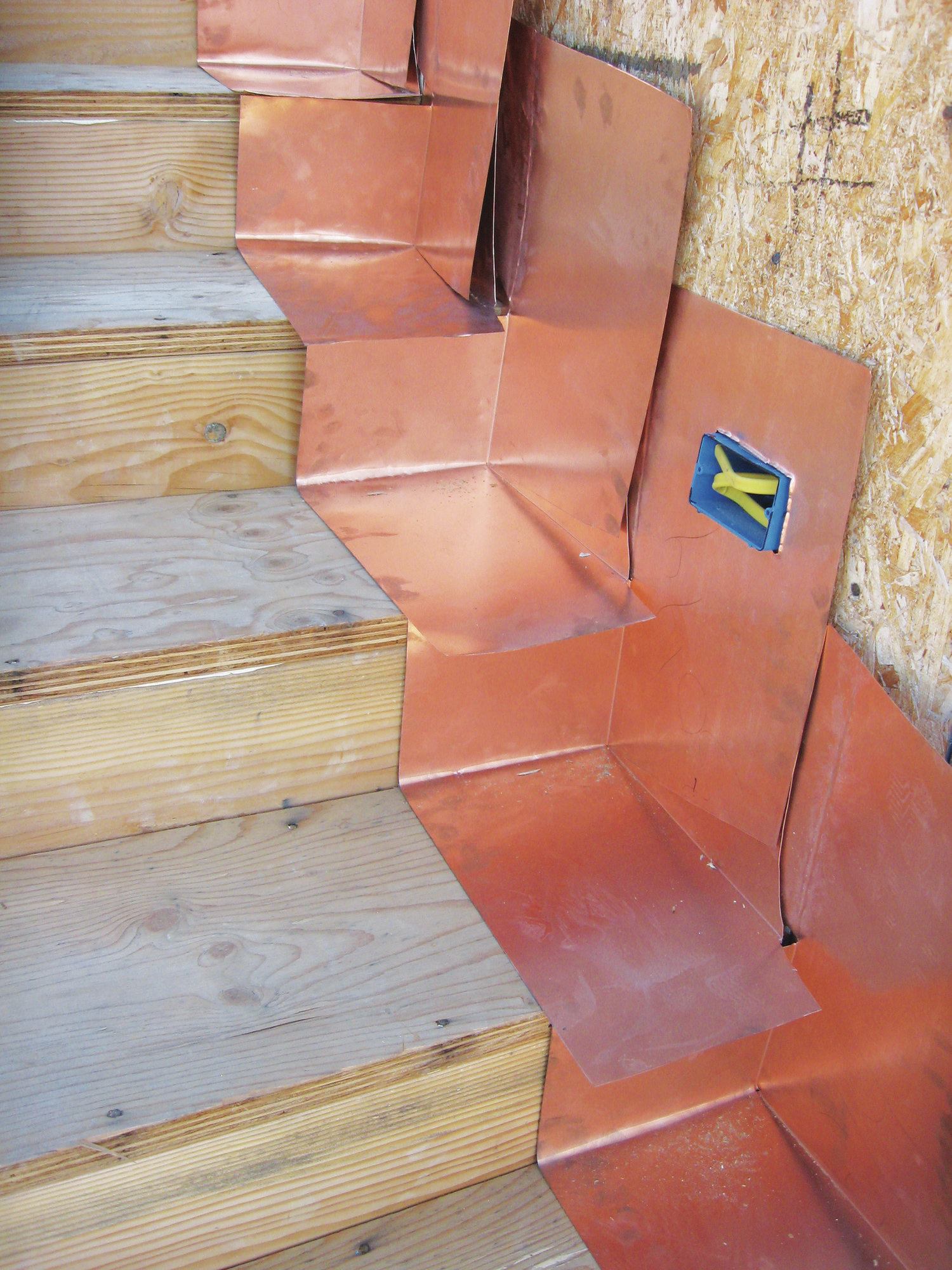 The copper stair flashing in the photo is just like deck flashing in miniature—when the cementitious deck coating is applied, it will completely cover the horizontal and vertical legs of the flashing.