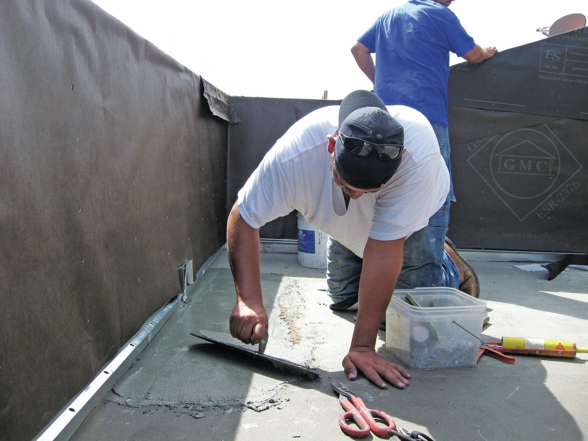 Cementitious coatings like Desert Crete are applied over metal lath stapled to the plywood sheathing. Chopped fiberglass mat is then glued to the base coat with acrylic resin, which acts as an anti-fracture and waterproofing membrane. After it dries, a protective screed coat is applied, with additional material helping to slope the surface for drainage, as required.